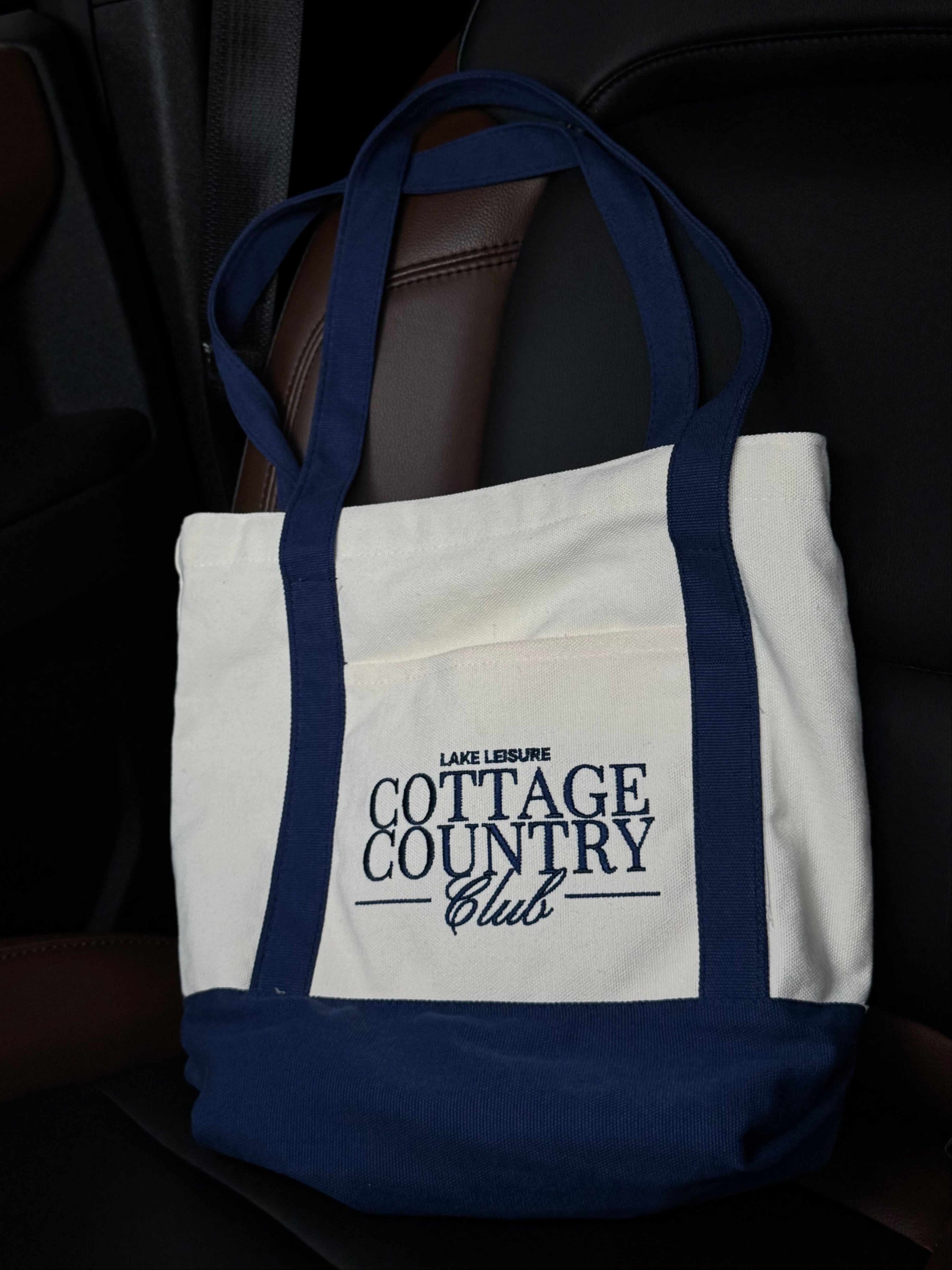 Tote bag with 'Cottage Country Club' text on a car seat
